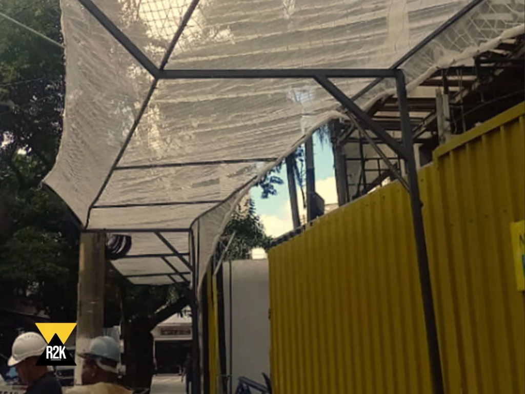 Estrutura de proteção de calçada instalada pela R2K em frente a um canteiro de obras, com telas e bandejas para garantir a segurança de pedestres contra queda de objetos.
