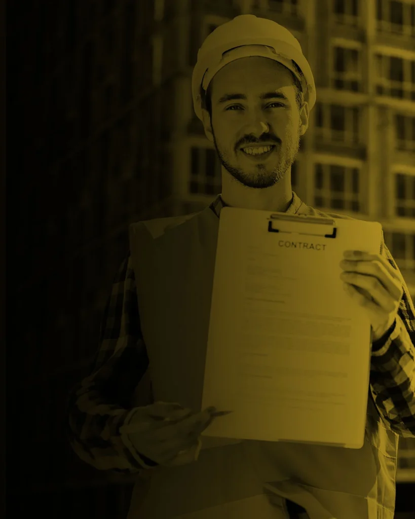 Engenheiro civil sorridente segurando prancheta de checklist em frente a um edifício em construção com sistemas de proteção coletiva.