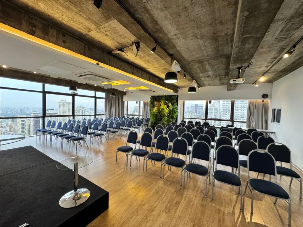 Auditório moderno no Espaço Essente, Avenida Paulista, preparado para o evento de Certificação R2K. Ambiente corporativo com vista panorâmica da cidade de São Paulo, cadeiras organizadas e estrutura premium para networking.