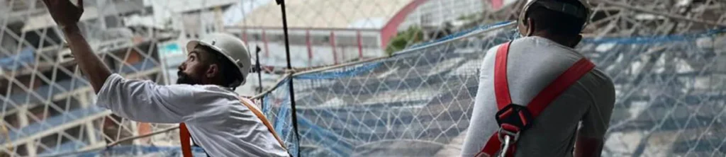 Equipe técnica da R2K realizando a instalação de rede de proteção piso a piso em estrutura de edifício, utilizando cintos de segurança e seguindo as normas NR-18 e NR-35.