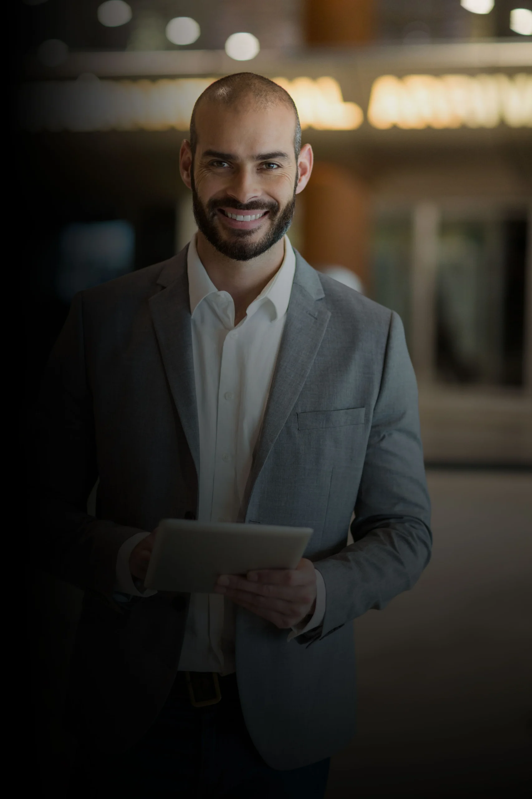 Homem sorrindo de terno cinza segurando um tablet, representando um consultor comercial moderno da R2K Proteção Coletiva.